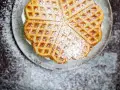 Herzförmige Waffeln, bestäubt mit Puderzucker, auf einem Teller. Ein köstliches Rezept für süße Momente.