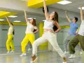 Grupa młodych ludzi ćwiczy taniec w sali z lustrami. Ich ruchy oddają energię gatunku muzycznego pop.