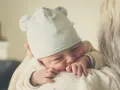 Nyfödd bebis med mössa med öron, tryggt vilande mot en axel. En perfekt baby gåva.