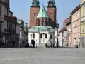 Spacer po brukowanym rynku Gniezna, z katedrą w tle. Kolorowe kamienice po bokach tworzą urokliwą atmosferę.