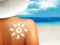 Słońce na plecach po opalaniu. Krem przeciwsłoneczny w kształcie słońca na skórze, plaża i morze w tle.