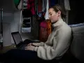 Ung kvinna sitter på golvet och jobbar på sin laptop, hon kombinerar studera på distans och jobba samtidigt.