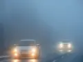 Dwa samochody jadące we mgle, z włączonymi światłami. Warto pamiętać o odpowiednich światłach do jazdy dziennej w takich warunkach.