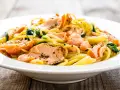 Deliciosa pasta con salmón desmenuzado y espinacas, servida en un plato blanco sobre una mesa de madera.