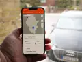 En hand håller upp en mobil med appen ChargeFinder som visar en karta över laddstationer för elbil. En laddapp visar en laddare nära en elbil.