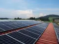 Duże panele PV na dachu budynku gospodarczego, otoczonego zielonymi wzgórzami.