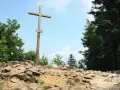 Drewniany krzyż na skalistym szczycie, najwyższy szczyt w górach świętokrzyskich, otoczony zielenią drzew.