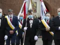 Rycerze Kolumba w garniturach i maskach maszerują z flagą.