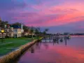 Beautiful waterfront homes and boats reflect a vibrant pink and purple sunset, perfect for weekend trips from Richmond, VA.