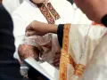 Ksiądz w bogato zdobionej szacie chrzci dziecko, polewając mu głowę wodą z kryształowej karafki.