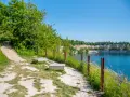 Ścieżka spacerowa nad turkusową wodą w kamieniołomie. Zakrzówek trasa zachęca do odpoczynku na ławkach wśród zieleni.