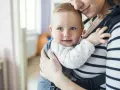 Uśmiechnięte dziecko w nosidle od urodzenia, przytulone do mamy.