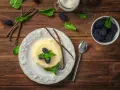 Budino fatto in casa alla vaniglia, guarnito con more fresche e menta. Ingredienti genuini per un dolce delizioso.
