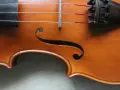 Drewniany korpus skrzypiec, z widocznymi strunami i mostkiem. Ten instrument, być może nawet stradiwarius, emanuje historią i pięknem.