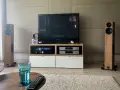 Dwie kolumny Audio Physic Virgo w drewnianej okleinie, telewizor, sprzęt audio i szklanka wody na stoliku.