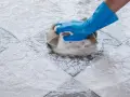 Mano con guanto blu che pulisce ceramica macchiata con spugna e schiuma.