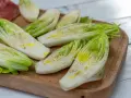 Insalata belga tagliata a metà, condita con olio e pepe, su un tagliere di legno.