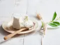 Świeża ricotta na drewnianej łyżce, obok kłosy zbóż i zielone gałązki. Idealna do dań, gdy szukasz czym zastąpić ricottę.