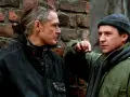 Dwóch mężczyzn rozmawia przy ceglanej ścianie. Jeden z nich, z siwymi włosami związanymi w kok, pali papierosa. Czy to rozmowa o tym, czym jest ekstradycja?