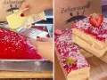 Ein leckerer Kuchen wird zubereitet. Butter wird über eine rote Masse gerieben, die an Spaghetti-Eis erinnert. Fertige Kuchenstücke mit Erdbeeren und Kokosraspeln sind zu sehen.
