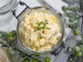 Cremiger Kartoffelsalat mit Fleischsalat, garniert mit frischen Kräutern, in einem Glas serviert.