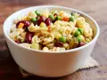 Una ciotola di pasta fredda con fagioli rossi, piselli, mais e cetriolini. Un piatto estivo perfetto.