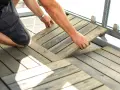 Mann legt Holzfliesen für den dachterrasse gestalten boden. Die Holzoptik passt gut zu modernen Außenbereichen.