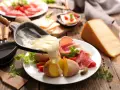 Roztopiony ser z patelni do raclette spływa na ziemniaki i wędliny. Pyszne danie raclette.