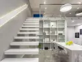 Nowoczesna antresola z białymi, lewitującymi schodami, przeszklonymi balustradami i minimalistycznym regałem.