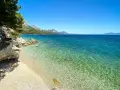 Idealne miejsce na camping w Chorwacji: kamienista plaża, turkusowa woda i góry w tle.