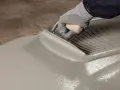 Mano guantata stende uno strato uniforme di Mapelastic, un materiale che si può lasciare a vista, creando una superficie liscia e pronta per ogni finitura.
