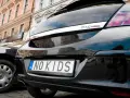 Czarne auto z indywidualnymi tablicami rejestracyjnymi "NO KIDS" na tle kamienicy.