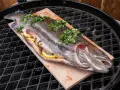 Lachsforelle auf einem Holzbrett, gefüllt mit Zitrone und Kräutern, bereit für den Grill. Die Kerntemperatur ist entscheidend für perfekten Fisch.