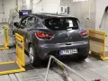 A dark grey Renault Clio is on a dynamometer in a testing facility, with exhaust pipes connected.