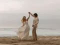 Coppia felice balla sulla spiaggia. Lui indossa un completo chiaro, perfetto per un matrimonio in spiaggia come vestirsi uomo.
