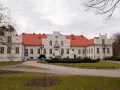Pałac Przebendowskich w Wejherowie, z czerwonym dachem i kremową fasadą, otoczony zielenią i drzewami.