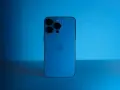 Elegancki iPhone 13 granatowy z potrójnym aparatem, lśniącym na tle niebieskiego światła.