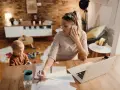 Mujer trabajando en casa con su hijo jugando cerca. Una escena de adaptación de jornada por cuidado de hijos, conciliando trabajo y familia.