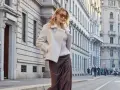 Donna con cappotto bianco in stile teddy, gonna di seta marrone e occhiali da sole, passeggia in città. Il **capispalla** è un elemento chiave per definire lo stile.