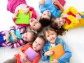 Dzieci leżą w kółku, trzymając kolorowe książki. Wszyscy uśmiechają się, gotowi do nauki. WWR!
