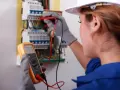 Elektryk wykonuje pomiary elektryczne w domu jednorodzinnym, używając multimetru do sprawdzenia instalacji.