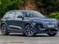 Elegancki, ciemnoniebieski Audi Q6 e-tron stoi na tle zieleni.