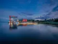 Nowoczesny hotel na ptasiej wyspie, otoczony spokojną wodą i zielenią, z łodziami przy pomoście.