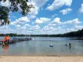 Sommerfreude im Strandbad Heiligensee: Kinder planschen, ein Mann kühlt sich ab, eine Rutsche lockt. Blauer Himmel mit weißen Wolken.