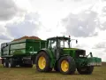 Zielony traktor John Deere z przyczepą wypełnioną ziemniakami na polu.