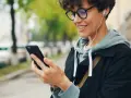 Uśmiechnięta osoba w słuchawkach patrzy na telefon. Czy wiesz, co to jest impedancja w słuchawkach i jak wpływa na dźwięk?