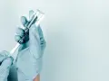Ręce w niebieskich rękawiczkach pobierają płyn do strzykawki z fiolki. Przygotowanie do podania milgamma zastrzyki.