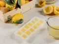 Frische Zitronen und eine Eiswürfelform gefüllt mit Zitronensaft zeigen, dass man Zitronen einfrieren kann.