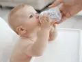 Niemowlę pije wodę z butelki. To idealne co do picia dla niemowlaka, gdy jest spragnione.