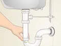 A hand loosens a pipe fitting under a sink, showing how to remove sink stopper.